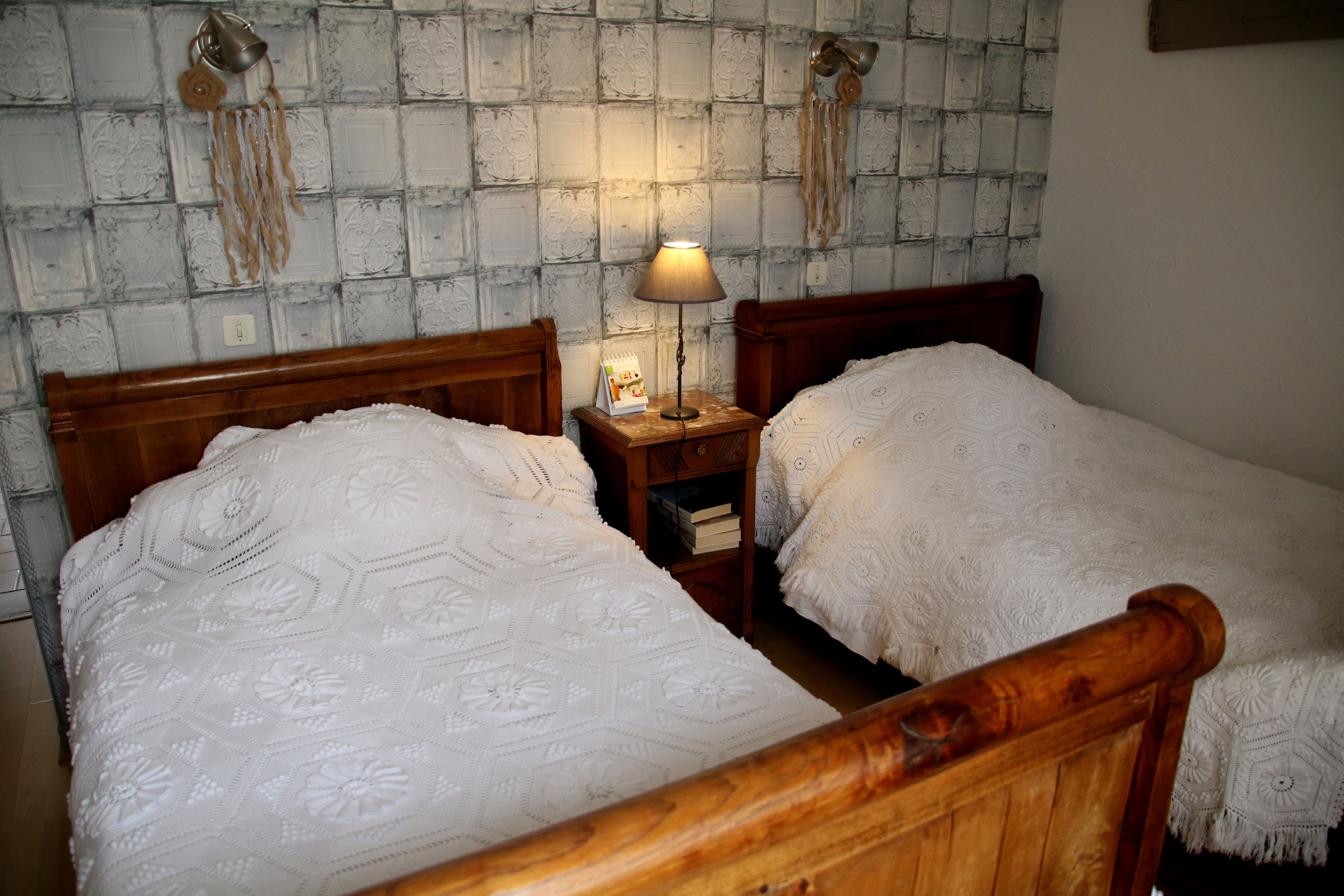 Una habitación con dos camas de madera, una mesita de noche con lámpara y una pared con textura.