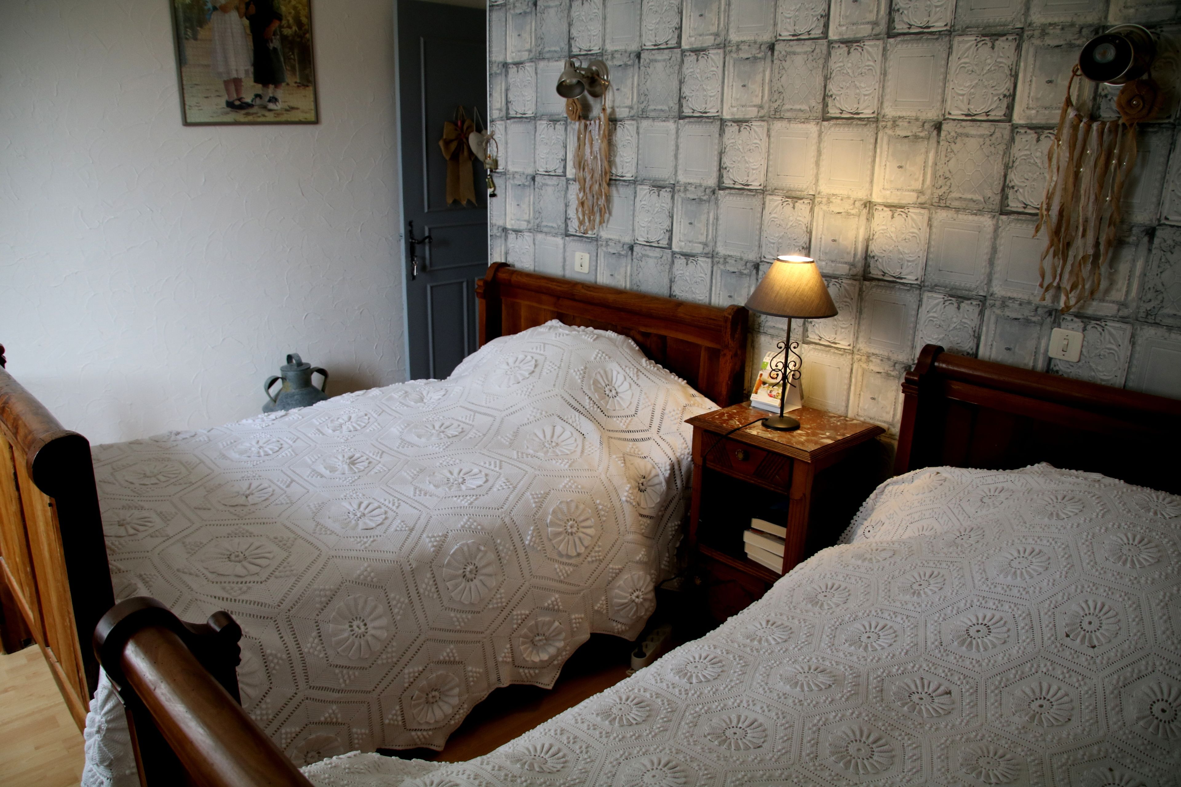A bedroom with two beds, a wooden headboard, a bedside table with a lamp, and a patterned wall.