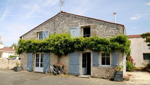 Un bâtiment en pierre avec un toit en pente, un vélo garé à l’extérieur et un petit jardin agrémenté de verdure.