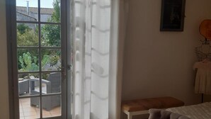 Une pièce avec un plancher en bois, un canapé gris avec un coussin, une petite table, une chaise et une porte donnant sur un patio extérieur.
