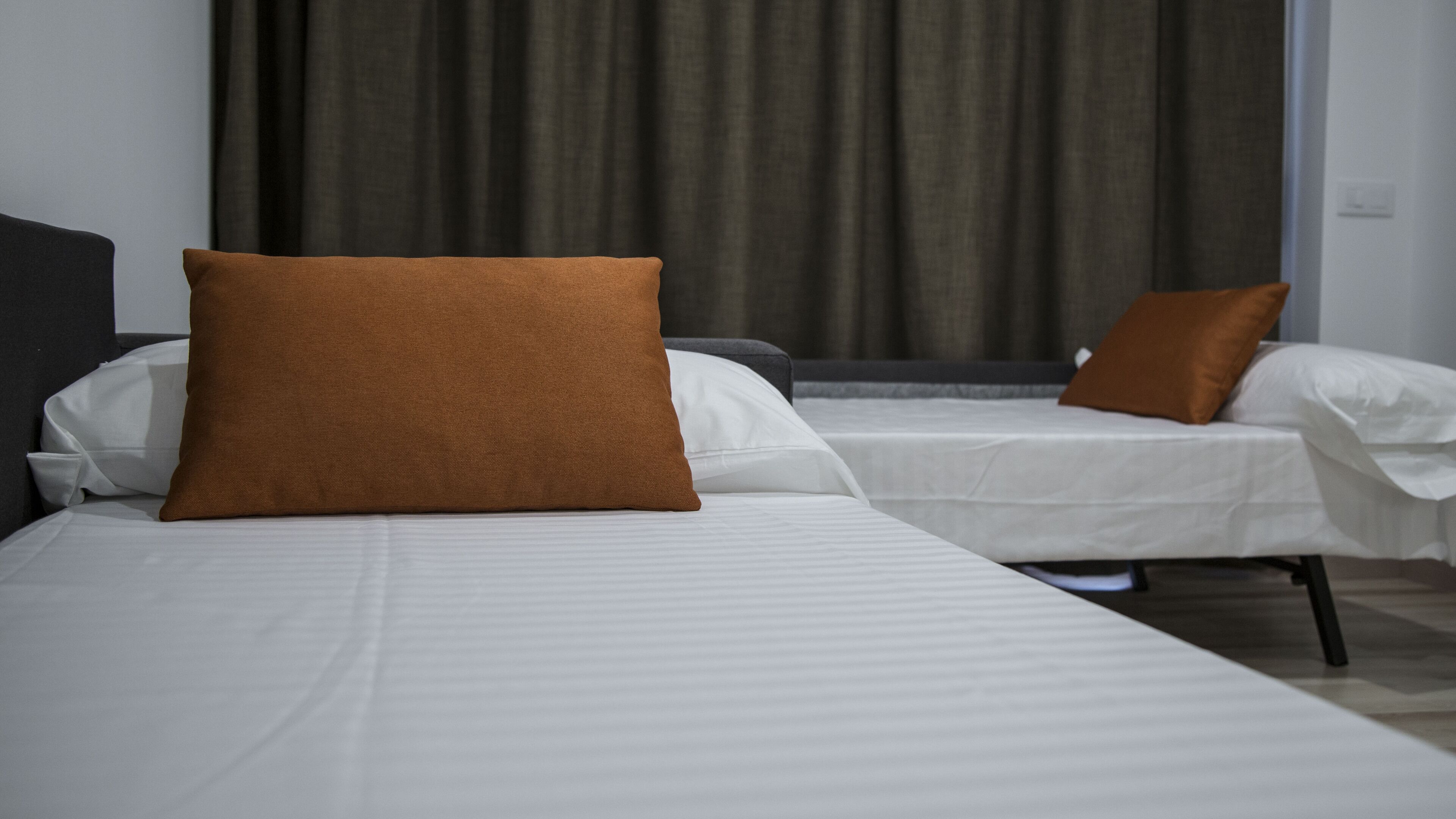 Ein Hotelzimmer mit zwei Betten, jedes mit einem braunen Kopfkissen und weißer Bettwäsche.