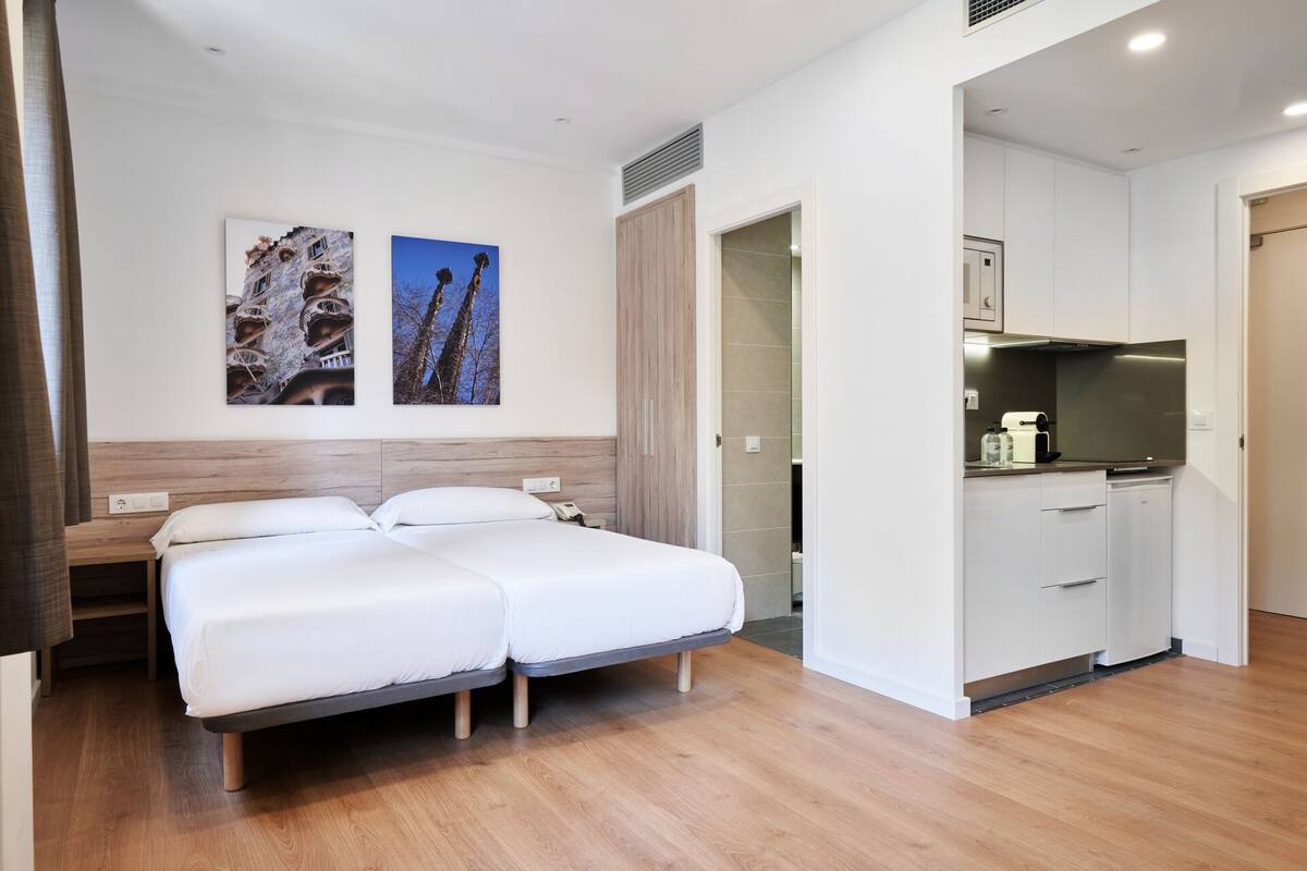 A hotel room with a bed, a kitchenette, and two wall-mounted artworks.