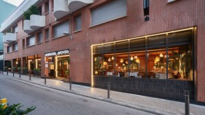 Un hotel moderno con fachada de ladrillo, ventanas grandes y mesas exteriores visibles desde el interior.