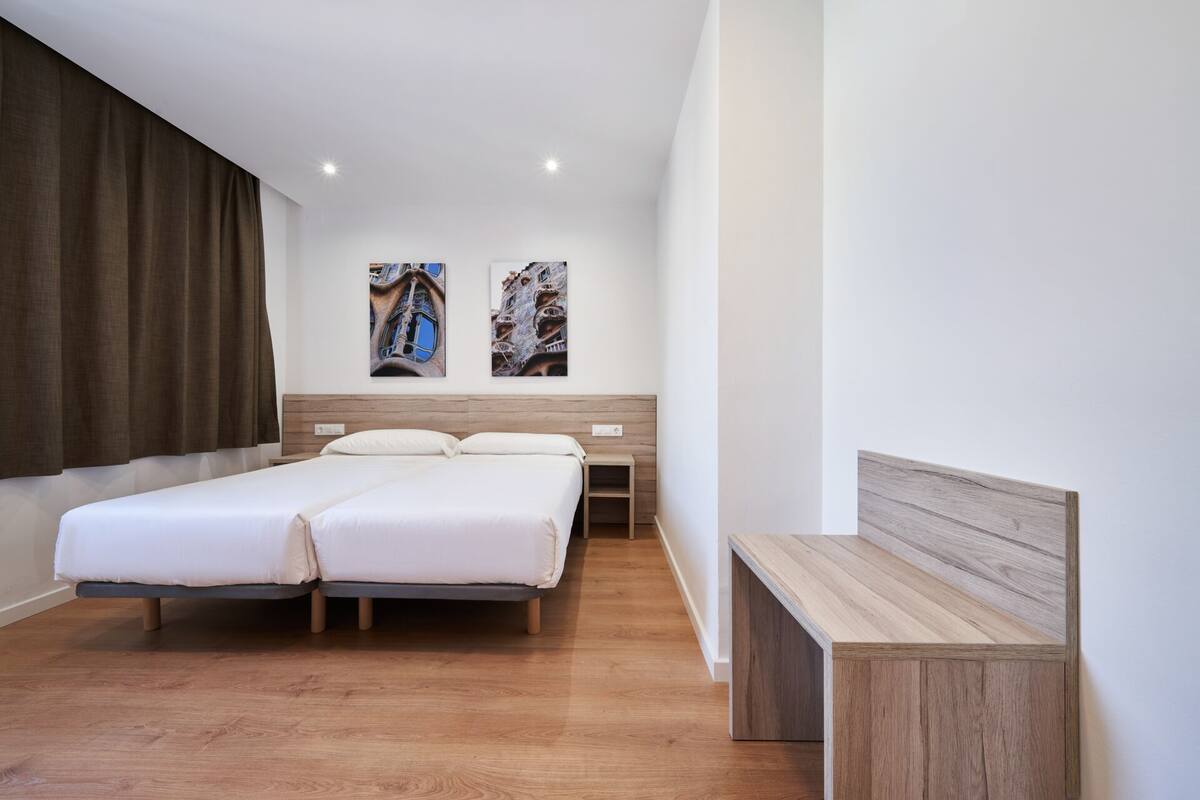 A modern hotel room with a double bed, a wooden bench, and two wall-mounted artworks.