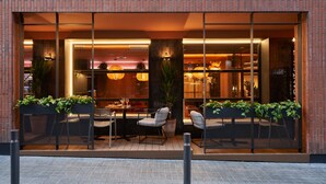 Un restaurante moderno con fachada de ladrillo, grandes ventanales y mesas y sillas para comer adentro.