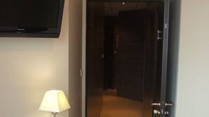 Une chambre d’hôtel équipée d’un téléviseur à écran plat fixé au mur, d’une lampe de chevet et d’une porte donnant sur une autre pièce.