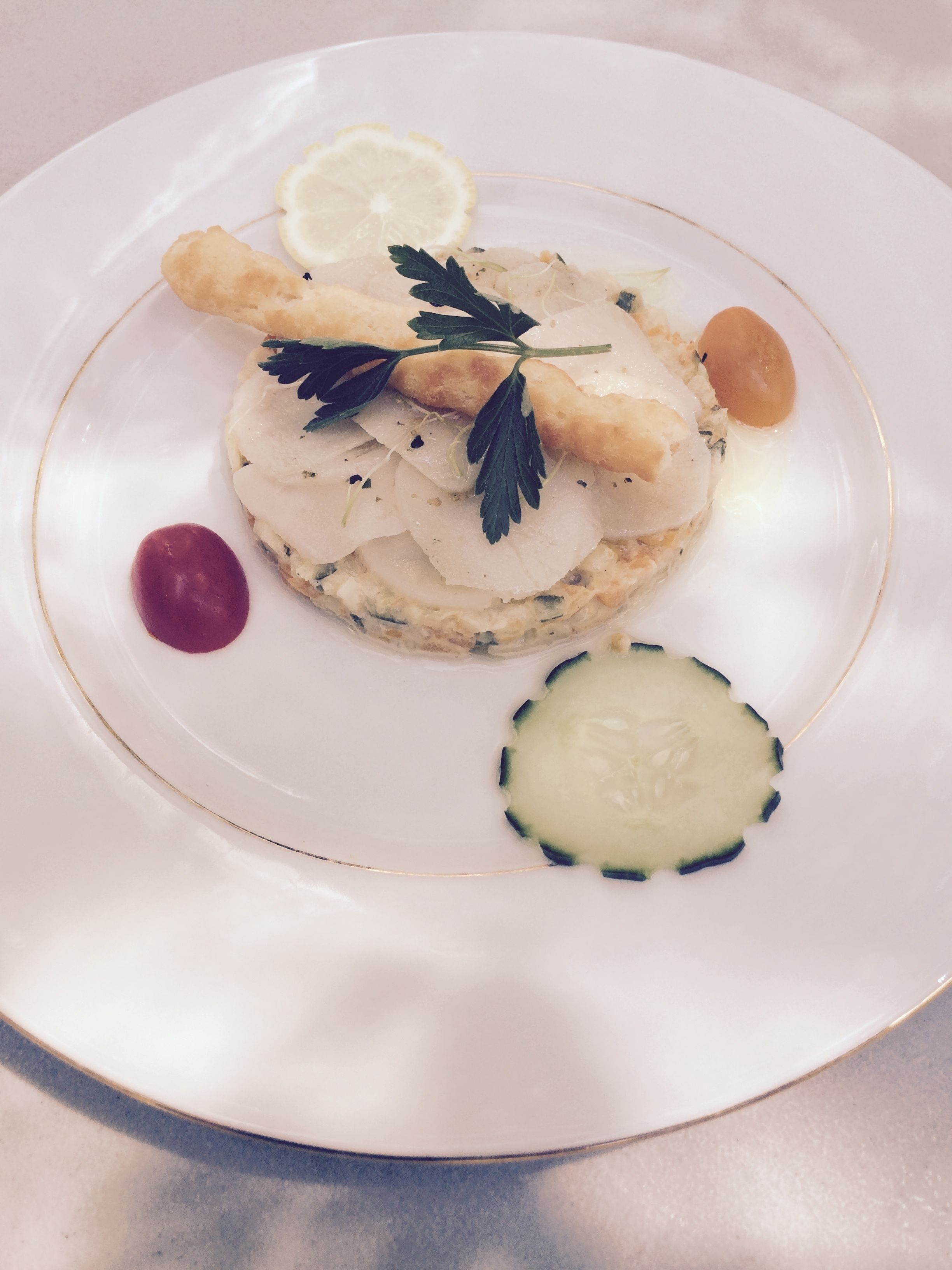 A plate with a layered seafood dish, garnished with herbs and lemon slices.