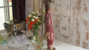 Une table avec une lampe, un vase rempli de fleurs, un gros morceau de viande et une planche à découper avec de la viande tranchée.