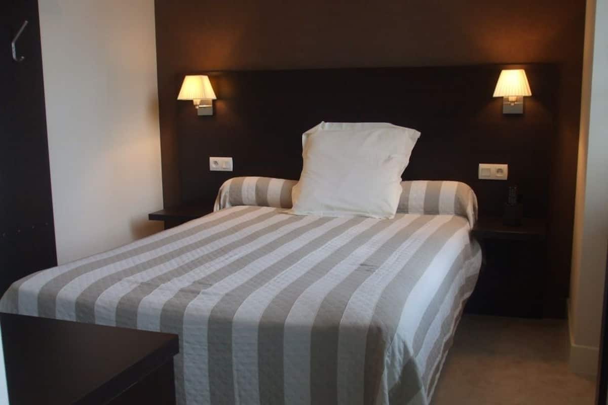A neatly made bed with striped bedding, two bedside lamps, and a dark headboard.
