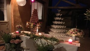 Une table dressée avec un gâteau à étages, de la verrerie, des bougies et des plantes en pot.