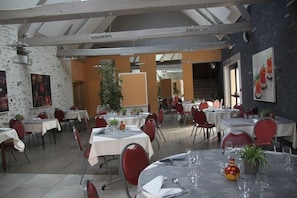 Un restaurant avec de nombreuses tables et chaises, un escalier en arrière-plan et un mélange de murs en pierre et de murs peints.