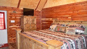 Een slaapkamer in een houten hut met een bed, een kaptafel en een televisie.
