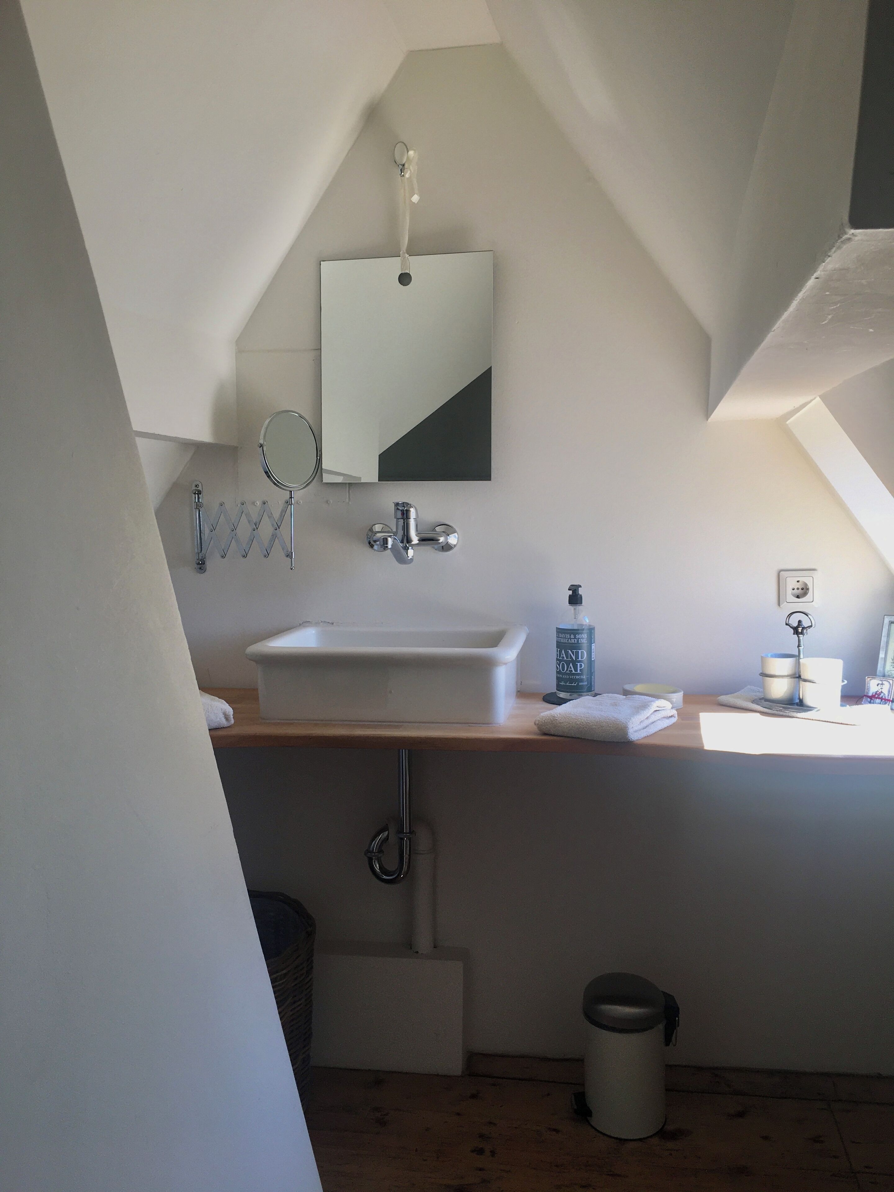A bathroom with a white sink, mirror, and towel rack. There is a bottle of hand soap on the counter.