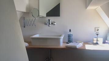 A bathroom with a white sink, mirror, and towel rack. There is a bottle of hand soap on the counter.