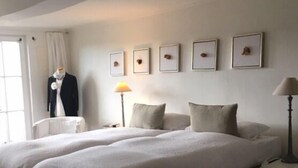 Een tweepersoonsbed met een neutraal kleurenpalet, een etalagemodel in een pak en ingelijste foto's aan de muur.