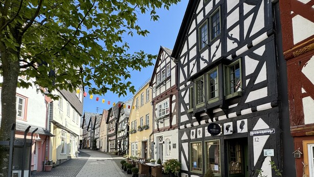 Een geplaveid straatje omzoomd door traditionele vakwerkhuizen, waarvan sommige borden en terrassen hebben.