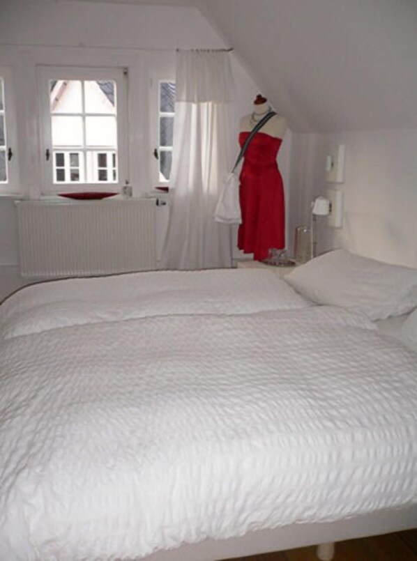 A bedroom with a large bed, a white radiator, a window with white curtains, and a mannequin in a red dress. - Boutiquehotel 14 (Hachenburg)