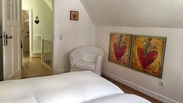 A bedroom with a large bed, a white chair, and two heart-themed paintings on the wall.