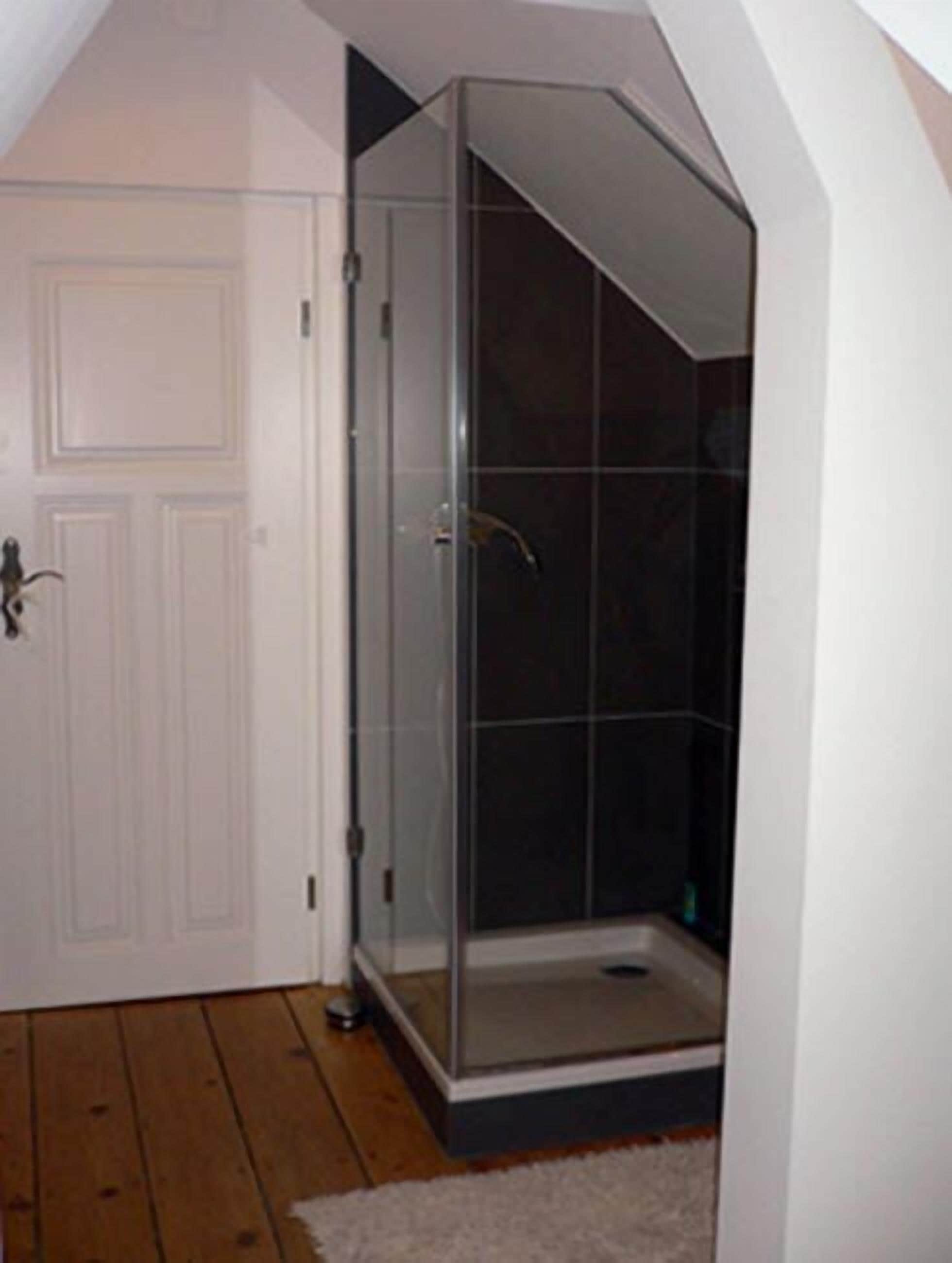 Ein Zimmer mit einer gläsernen Duschkabine, einer weißen Tür und Holzboden.