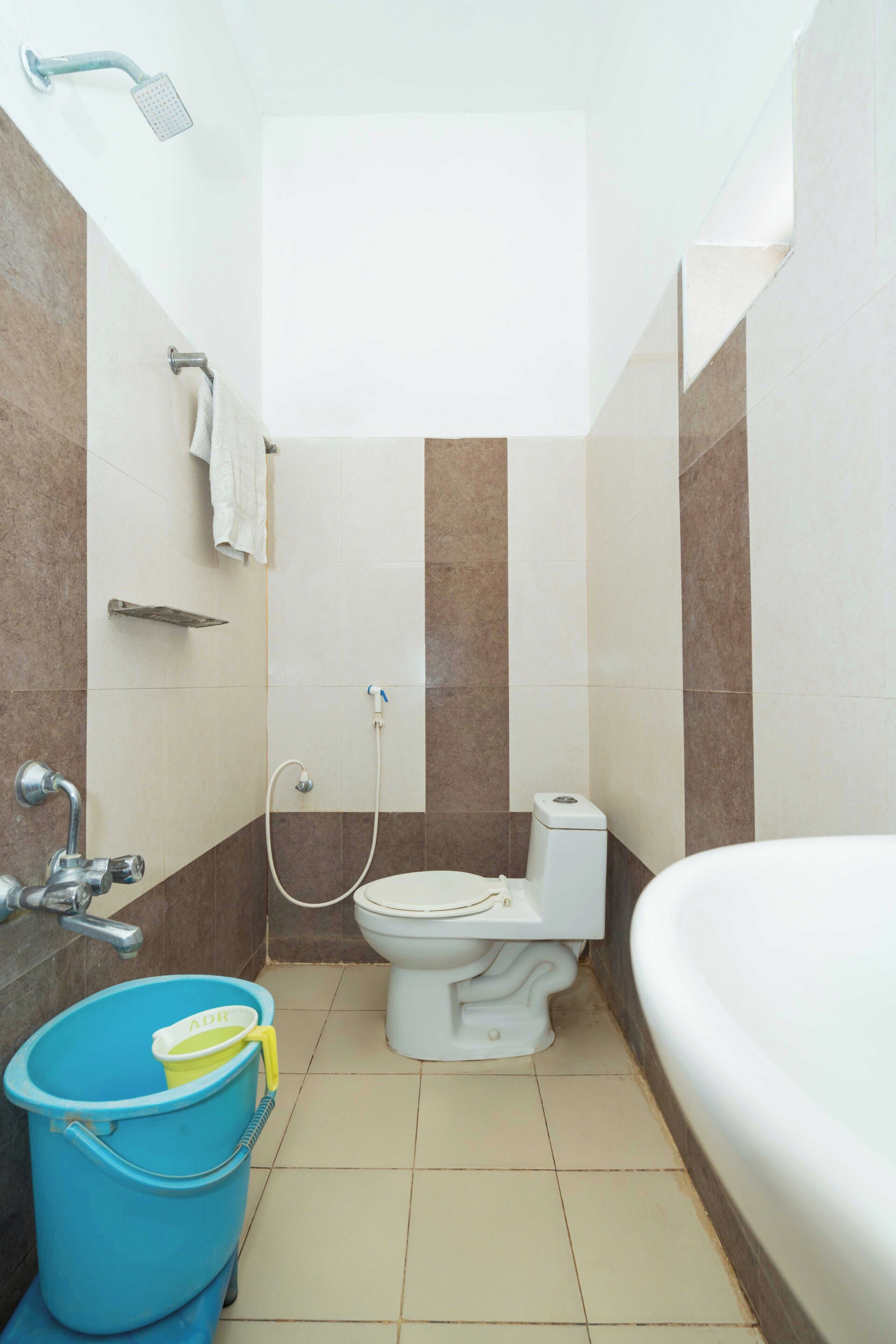 A bathroom with a toilet, bidet, bathtub, and a blue bucket.