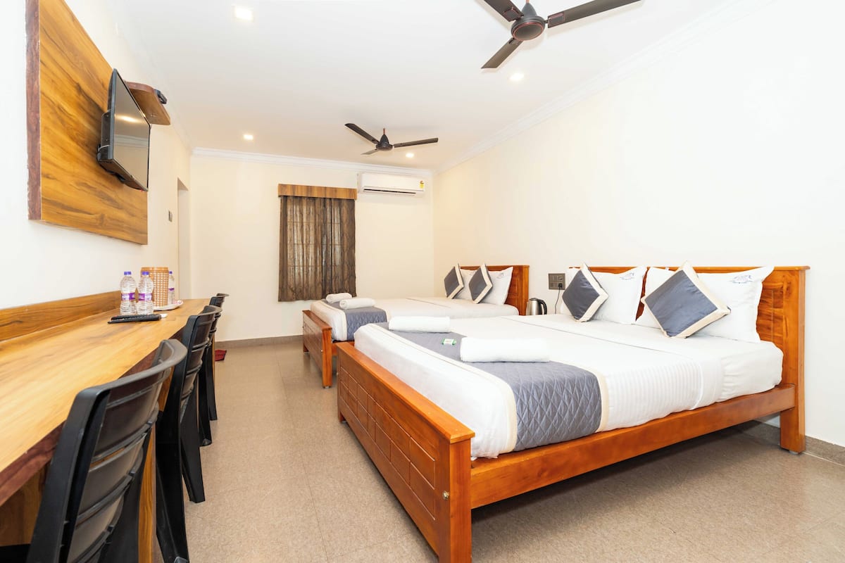 A hotel room with a wooden bed, a desk with chairs, a flat-screen TV mounted on the wall, and ceiling fans.