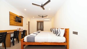 A hotel room with a large bed, a desk with chairs, a television mounted on the wall, and two ceiling fans. - Hotel NNP Grand (Rameshwaram)