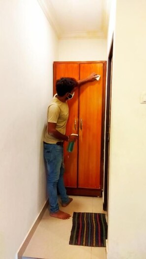 Una persona limpiando una puerta de madera en un pasillo estrecho con un tapete a rayas en el suelo.
