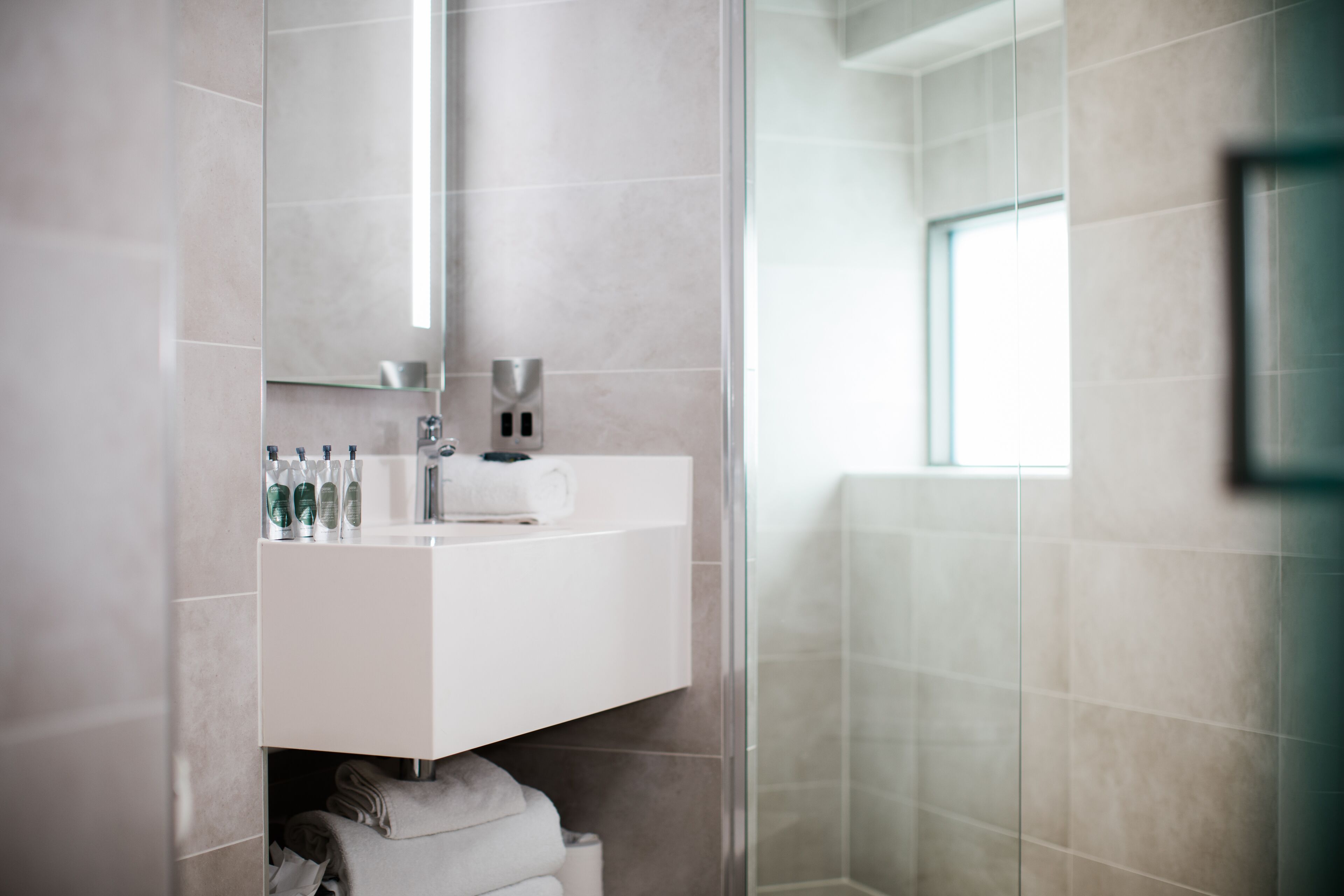 A modern bathroom with a glass shower enclosure, a white vanity with toiletries, and a large mirror.