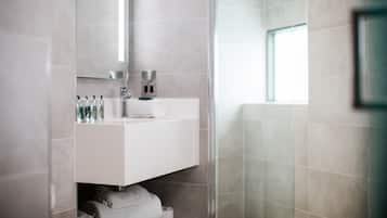 A modern bathroom with a glass shower enclosure, a white vanity with toiletries, and a large mirror.