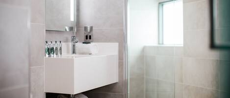 A modern bathroom with a glass shower enclosure, a white vanity with toiletries, and a large mirror.