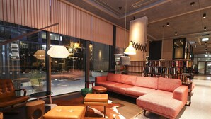 A modern interior with a red sofa, leather armchair, and ottomans, along with pendant lighting and a glass wall offering a view of the outside. - Marlin Hotel Stephens Green (Dublin)
