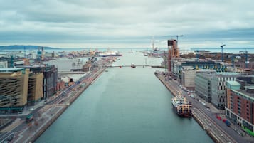 A waterfront cityscape with a large body of water, a bridge, and various buildings including a tall structure under construction.