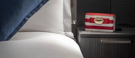 A neatly made bed with blue and white pillows, a bedside table with a lamp, and a red and white box on the table.