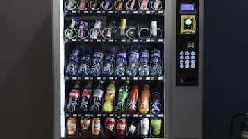 Máquina automática de vendas com diversos lanches e bebidas, incluindo batatas fritas, refrigerantes e água engarrafada.