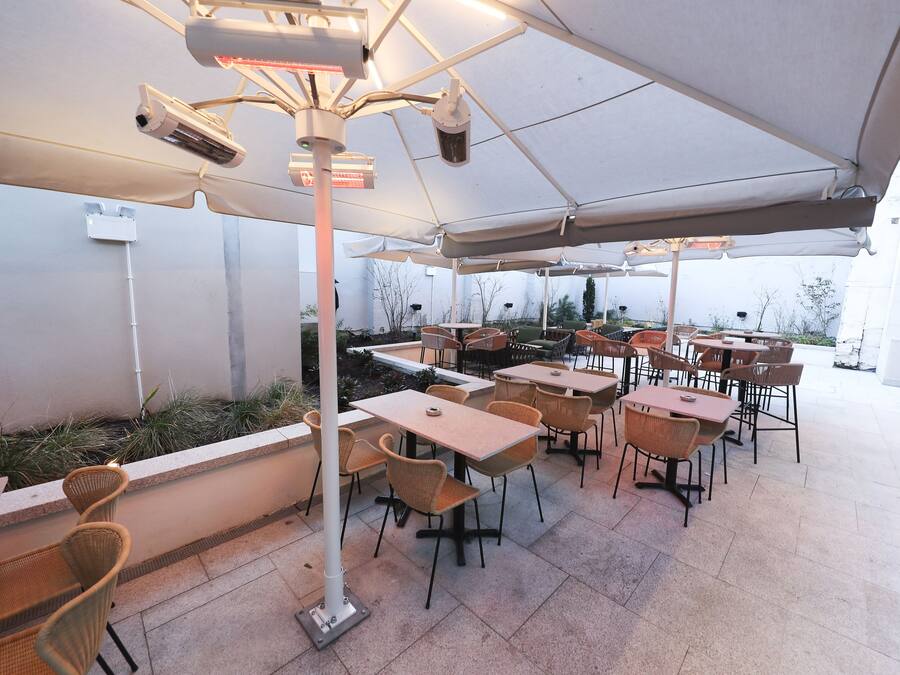 Un patio al aire libre con mesas y sillas, cubierto por un gran paraguas y equipado con lámparas de calor.