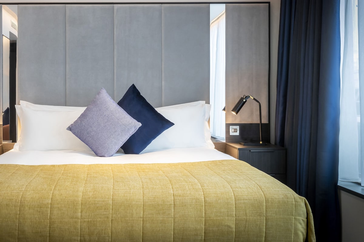 A neatly made bed with a yellow bedspread, two pillows, and a headboard.