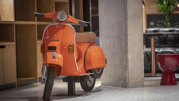 A vintage orange Vespa scooter parked indoors, near a concrete pillar and a red object.