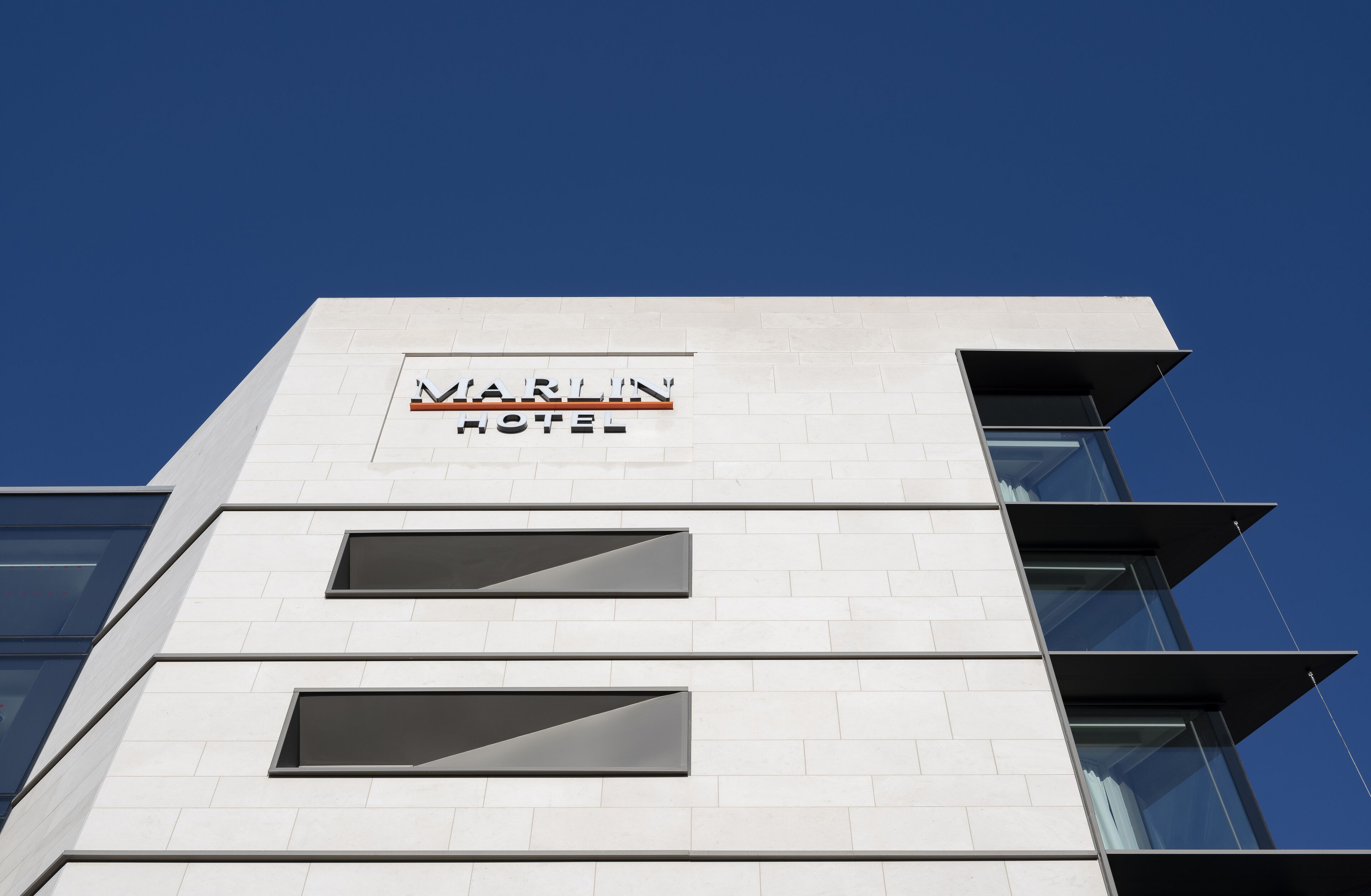 Ein MARLIN HOTEL Gebäude mit modernem architektonischen Design, das ein auffälliges Schild und große Fenster zeigt.