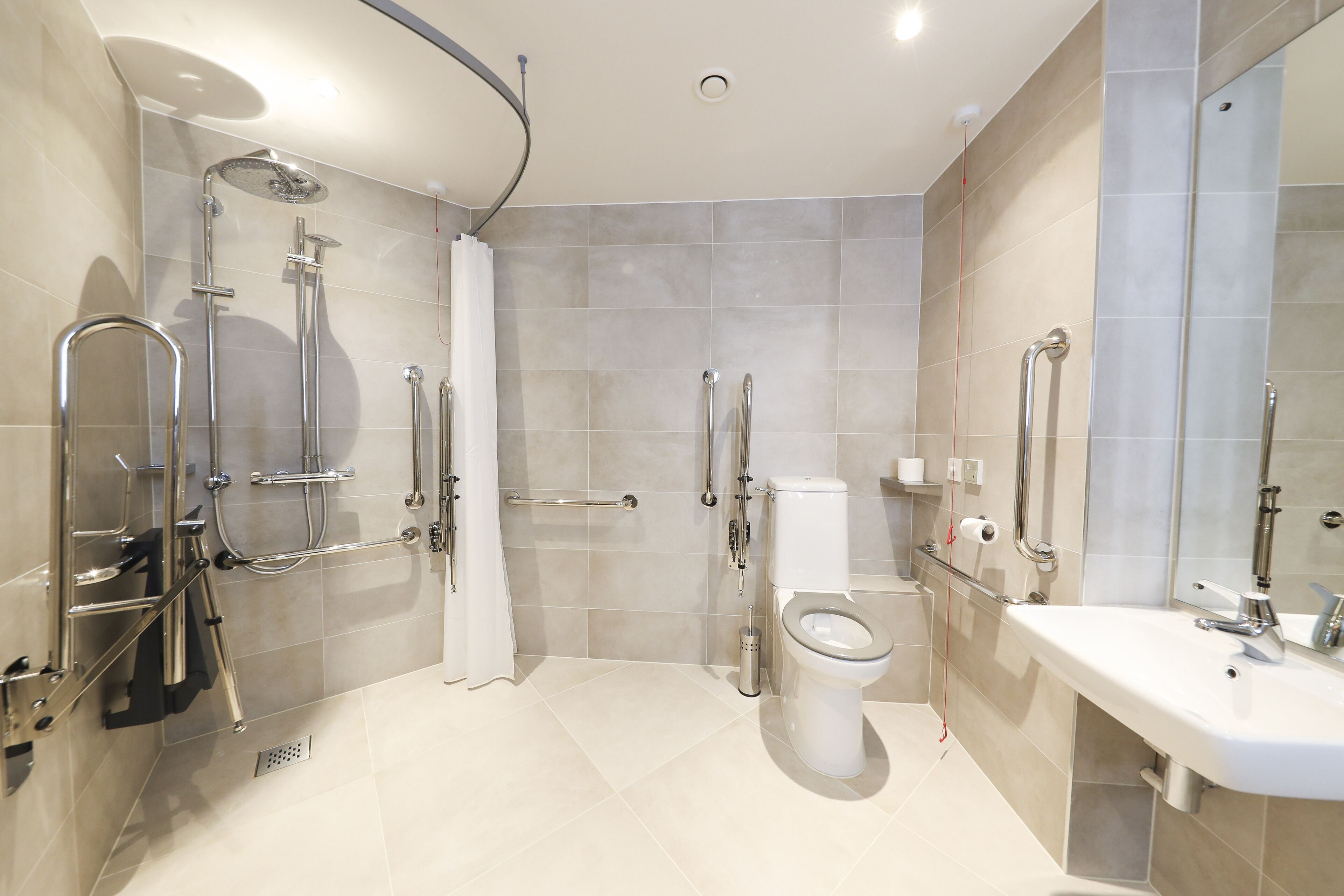 A modern bathroom with a shower, toilet, and sink, equipped with grab bars and a walk-in shower.