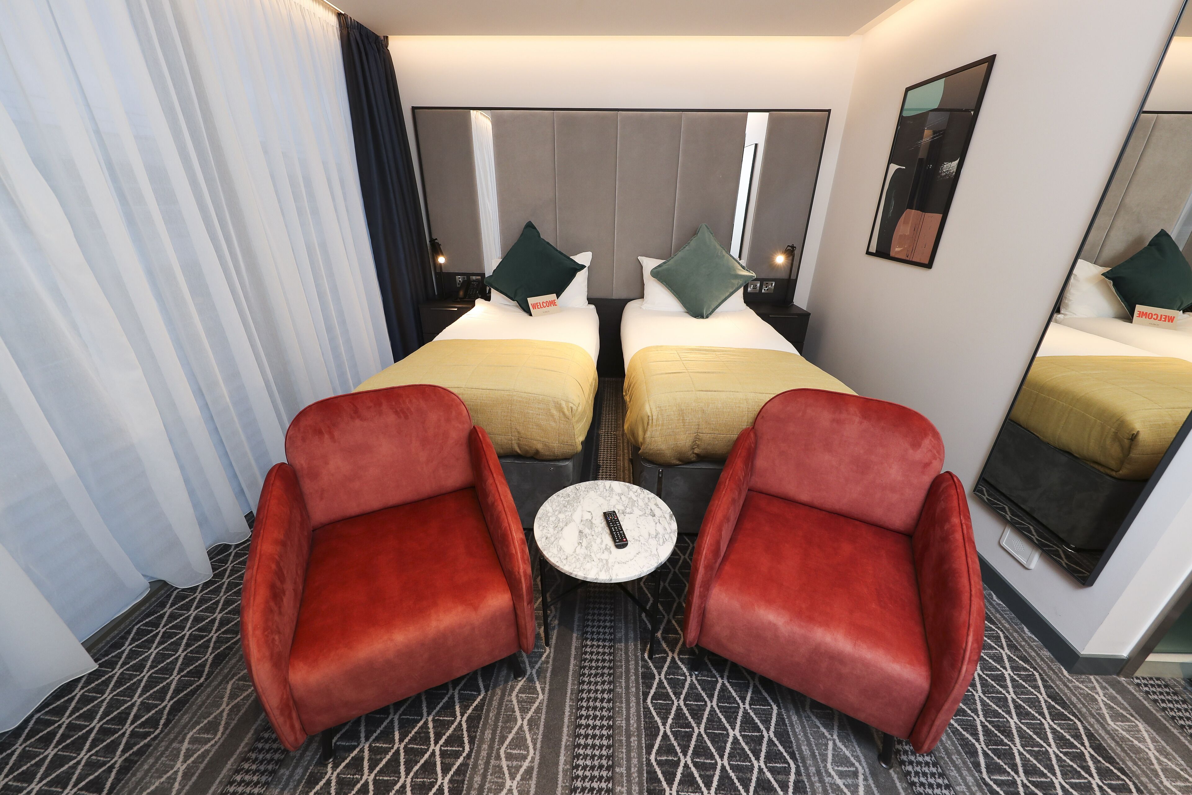 Ein Hotelzimmer mit zwei Betten, einem kleinen runden Tisch und zwei roten Sesseln.