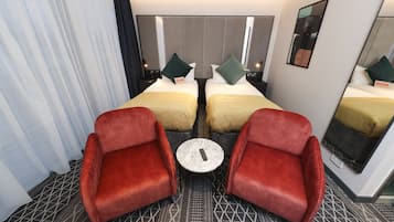 Ein Hotelzimmer mit zwei Betten, einem kleinen runden Tisch und zwei roten Sesseln.
