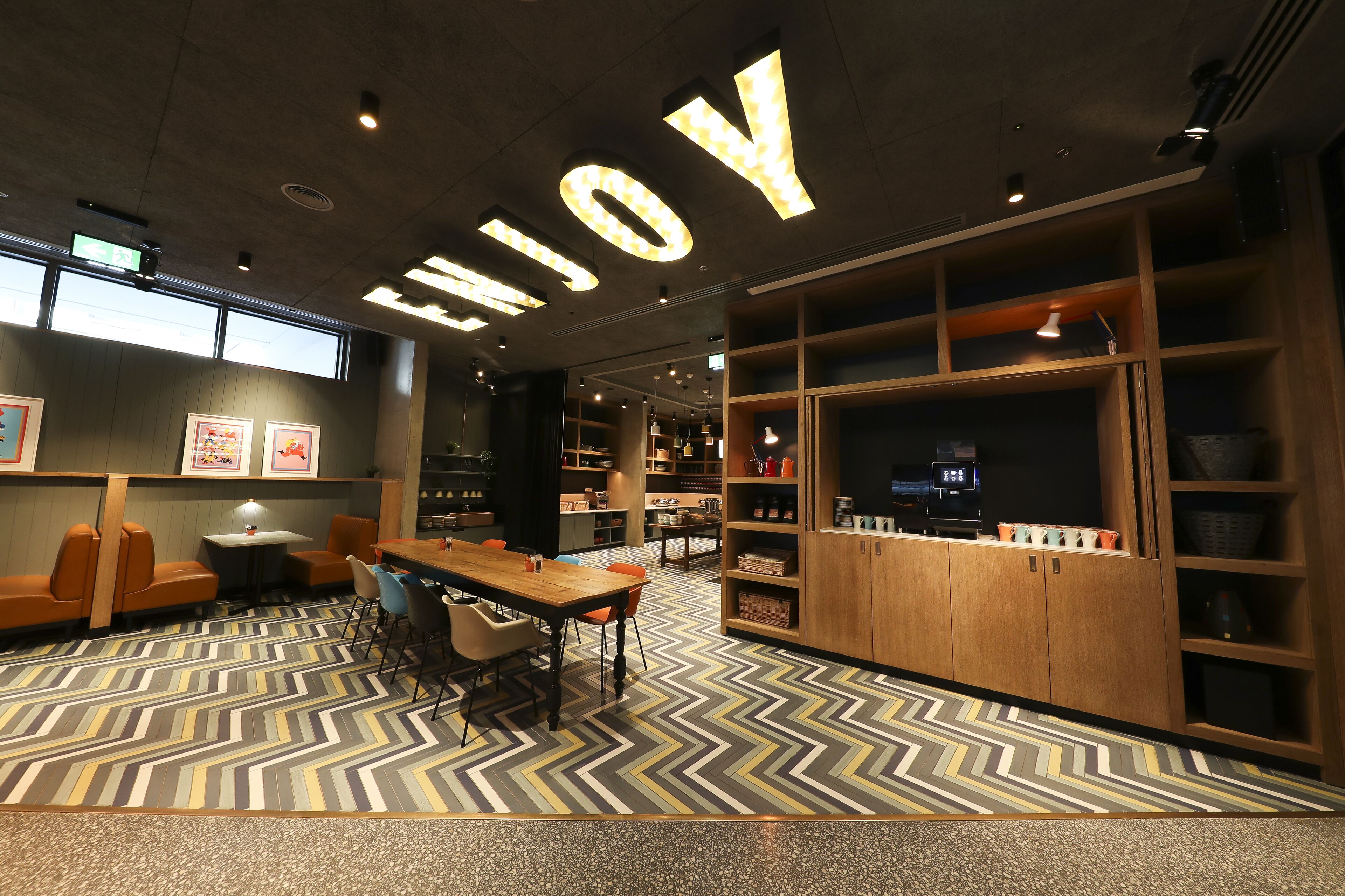 A modern library with a large 'ENJOY' sign, wooden bookshelves, and a patterned floor.