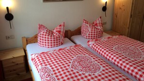 A double bed with checkered bedding, two bedside tables, a wall-mounted artwork, and a wooden wardrobe. - Pension Zum Bauernstübl (Meerane)