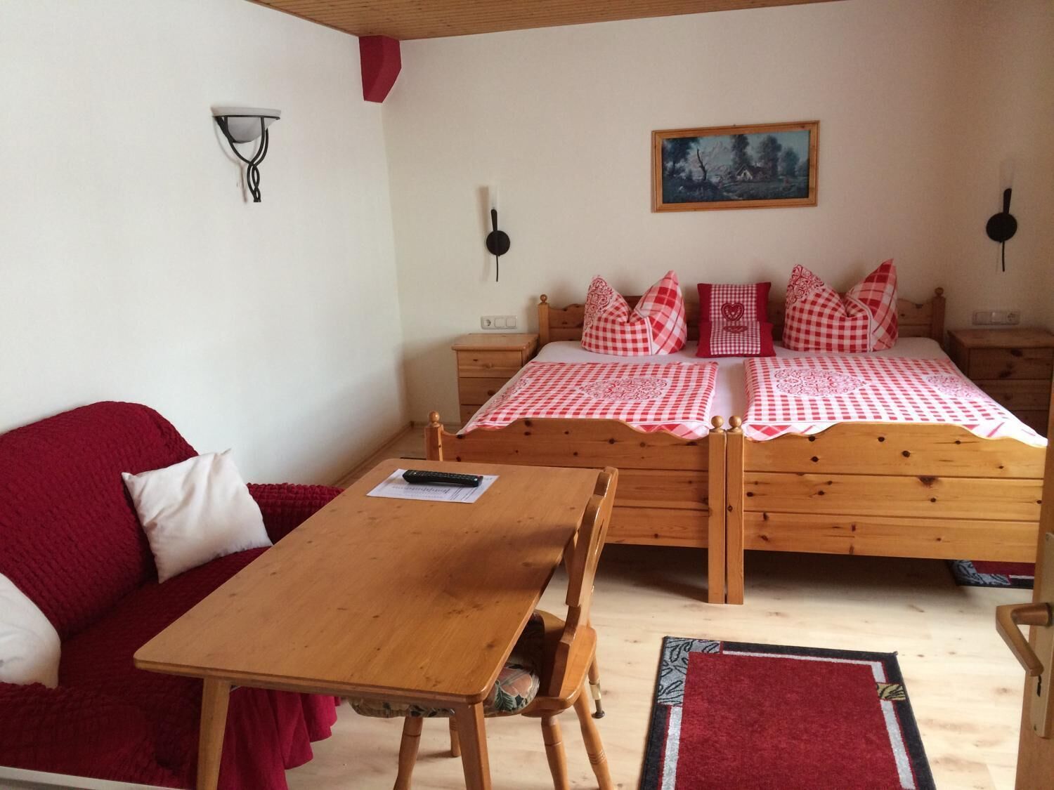 Une chambre confortable avec un lit en bois, un canapé rouge, une table en bois et un petit bureau.
