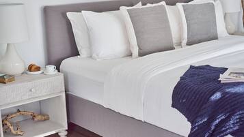 Una cama bien hecha con cabecera gris, ropa de cama blanca y una manta de color azul oscuro. Hay una mesita de noche con una lámpara, una taza y un libro.
