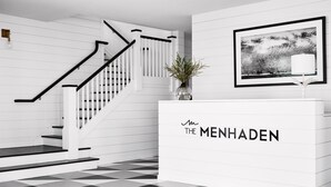Un área de recepción moderna con una escalera, una obra de arte enmarco y un mostrador de recepción con la señalización 'THE MENHADEN'.