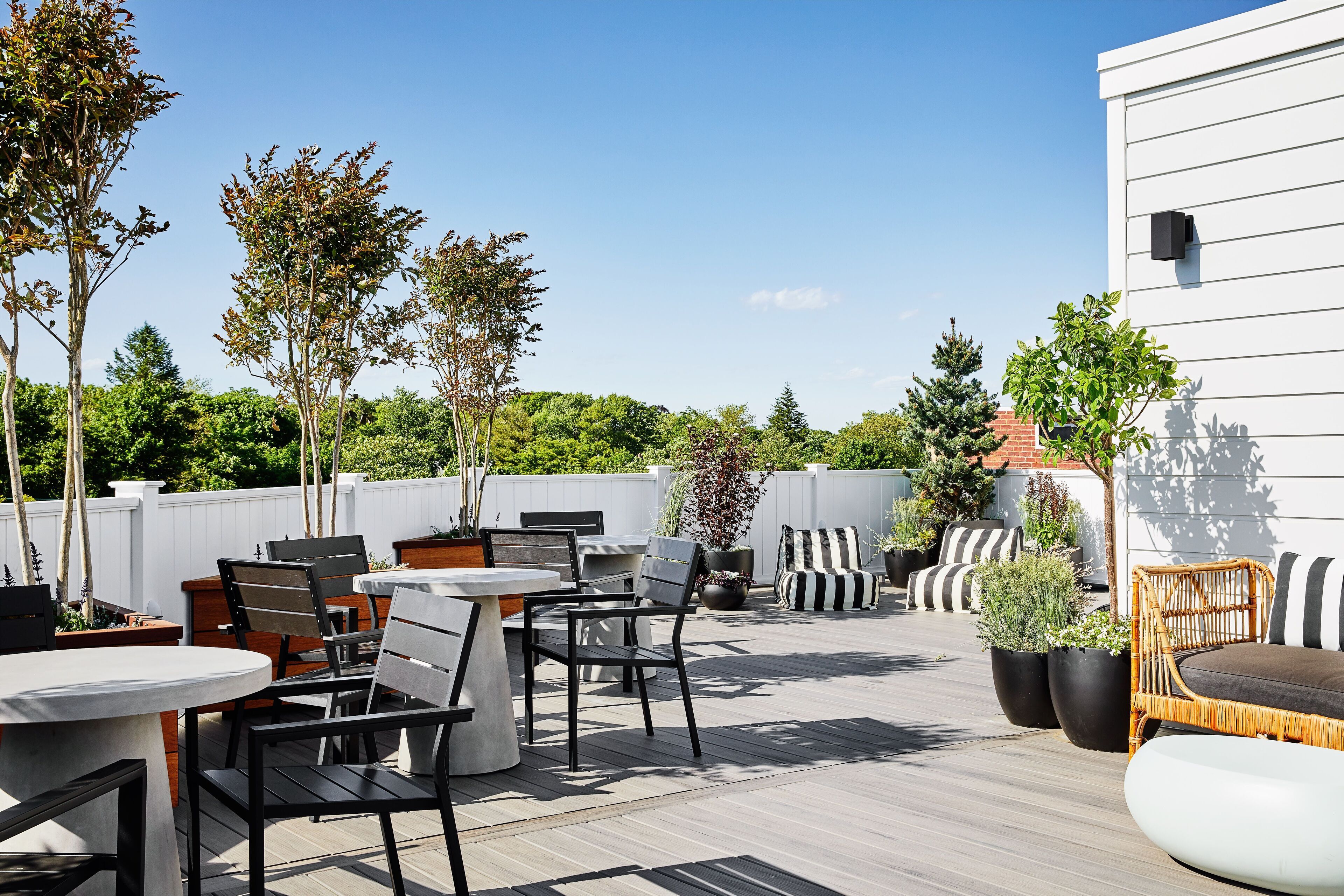 Un espace extérieur aménagé en terrasse, avec des tables et des chaises, des plantes en pot et un bâtiment blanc en arrière-plan.