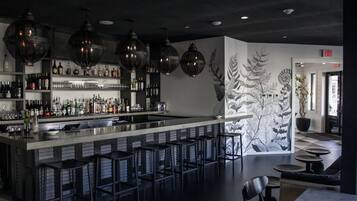 A bar area with a long counter, multiple stools, and hanging lights. There are shelves with bottles and glasses, and a mural on the wall.