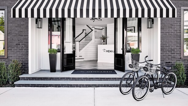 Entrada de un edificio moderno con un toldo a rayas negras y blancas, una escalera que da al interior y dos bicicletas estacionadas afuera.