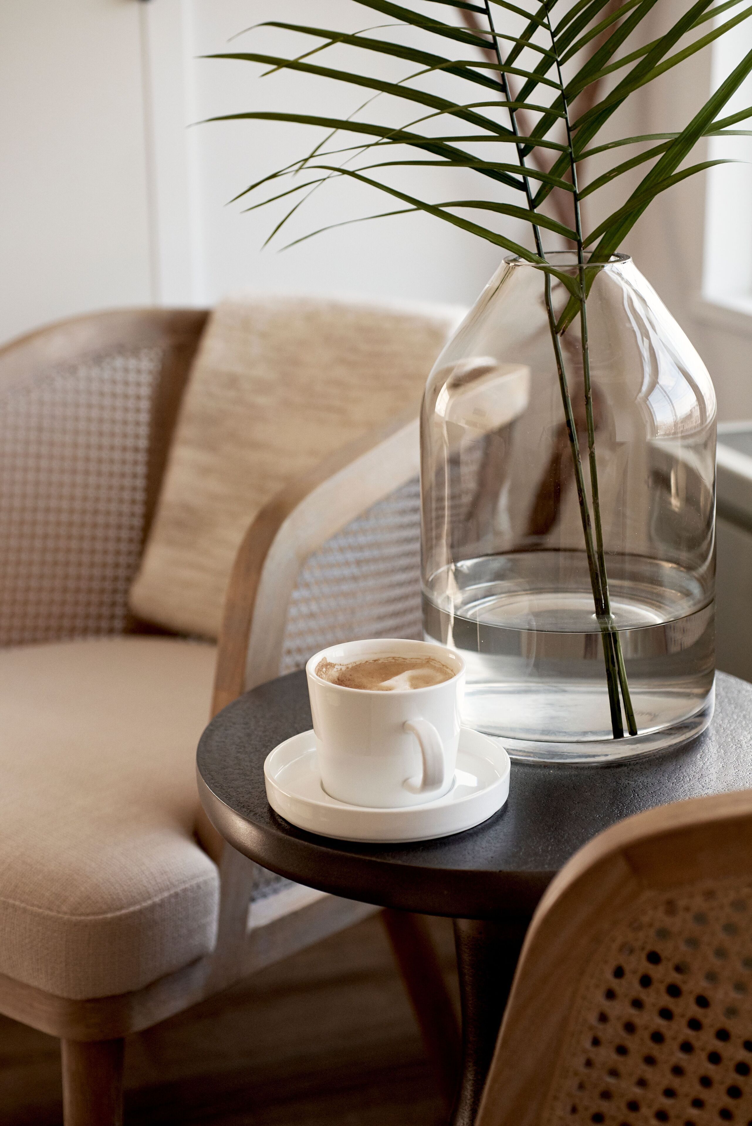 Un gerro de vidre transparent amb una planta sobre una taula, a prop d'una tassa de cafè.